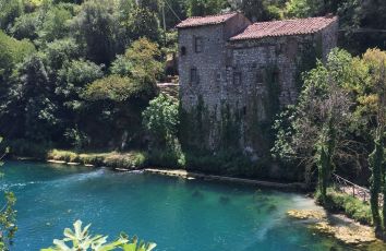 Un palazzo in pietra situato vicino a un lago, circondato dalla natura, con il riflesso nell'acqua turchese.