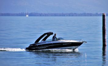 Una barca a motore di colore scuro naviga su un lago tranquillo, con un uomo alla guida.