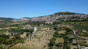 Panorama di una collina con edifici storici e campi coltivati, immersi nel verde della natura.