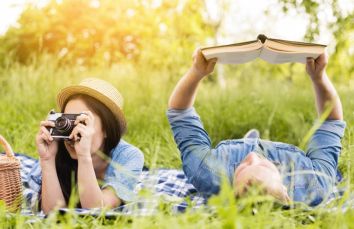 Una coppia trascorre una giornata tranquilla all'aperto, uno con una macchina fotografica e l'altro intento nella lettura di un libro.