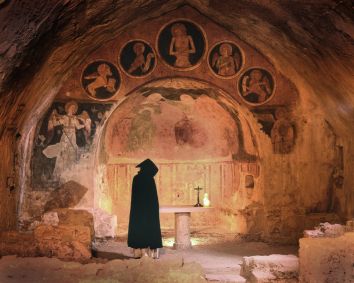 Un monaco osserva gli affreschi all'interno di una chiesa scavata nella roccia, creando un'atmosfera serena e storica.