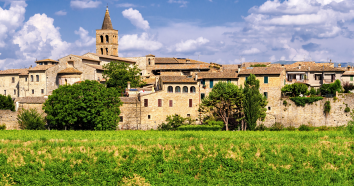 Una scena di un borgo storico con case in pietra e un campanile che si staglia contro un cielo azzurro.