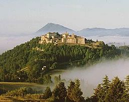 Panorama di un castello immerso nella nebbia e circondato da alberi.