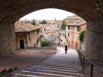 Una donna scende lungo una scalinata in un borgo storico, circondata da case tradizionali e un panorama caratteristico.