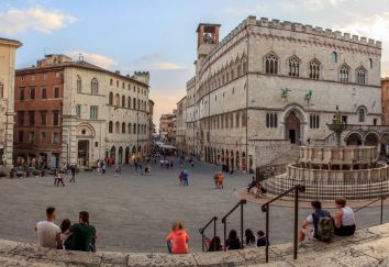 Piazza con palazzi storici e una fontana, frequentata da visitatori e abitanti.