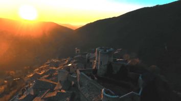 Un tramonto si riflette dolcemente su un borgo storico, circondato da colline verdi, creando un'atmosfera di serenità.