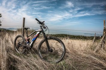 Una mountain bike poggiata su un prato secco con un panorama tranquillo e cielo azzurro sullo sfondo.