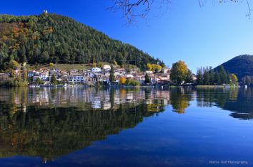 Un paesaggio tranquillo nei pressi di un lago, caratterizzato da riflessi della natura e del piccolo borgo circostante.