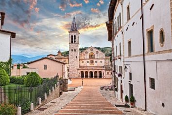 Panorama di un borgo in Umbria con una chiesa e un paesaggio montano visibile sullo sfondo.