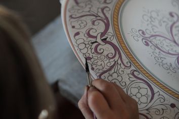 Un artista dipinge a mano su un pezzo di ceramica con dettagli raffinati.