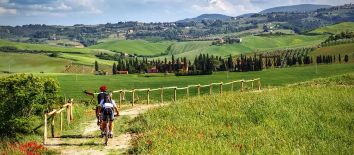 Vacanza attiva 5 giorni escursione in mountain bike nei dintorni di Assisi. Sportivamente Umbria - Umbria my love - Un gruppo di ciclisti percorre una tranquilla strada circondata da un paesaggio collinare verde e rigoglioso.