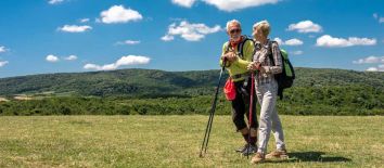 Vacanza all’aria aperta in Umbria hiking sul Monte Subasio con guida. Experience Umbria my Love - Due persone passeggiano in un contesto montano, sorridendo e conversando, immerse in un ambiente naturale.