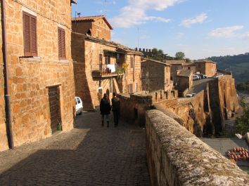 Una strada in un borgo storico con case in pietra e alcune persone che passeggiano.