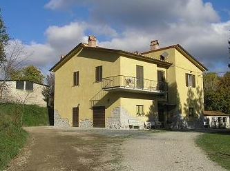 A yellow villa surrounded by trees, with a terrace overlooking a spacious garden.