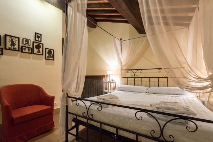 Interno di una camera semplice con letto a baldacchino e decorazioni d'epoca, adatta per un soggiorno tranquillo.