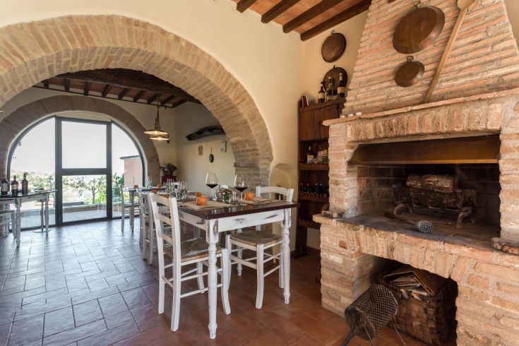 Una cucina calda con camino in mattoni e tavoli apparecchiati, affacciata su un panorama di campagna.