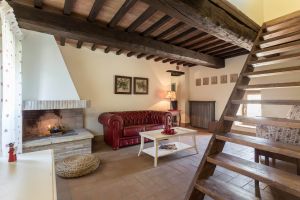 Soggiorno caldo con divano in pelle e camino, completato da travi in legno e una scala in legno chiaro.