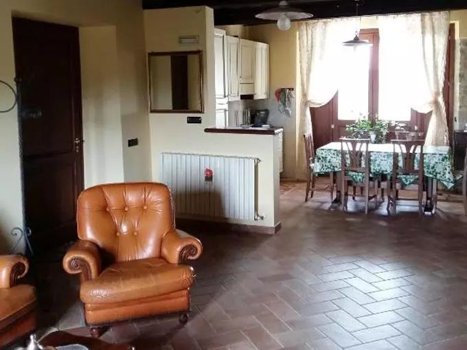 Interior of a farm stay with a cozy living area, lounge corner, and kitchen, featuring wooden furniture and terracotta floor.