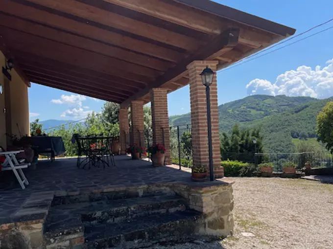 Country structure with a porch, surrounded by trees and green hills. A peaceful place to relax.