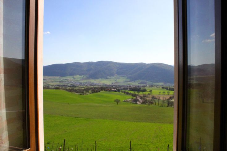 Panorama di colline verdi e montagne visibile da una finestra aperta di un casale.