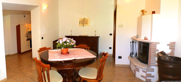 Spaziosa sala da pranzo in un casale con camino centrale e un semplice centro tavola di fiori freschi.