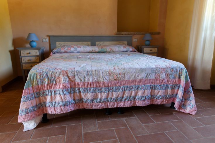 Ein helles Schlafzimmer mit einem Doppelbett und lebhaften Stoffen, schlicht eingerichtet.