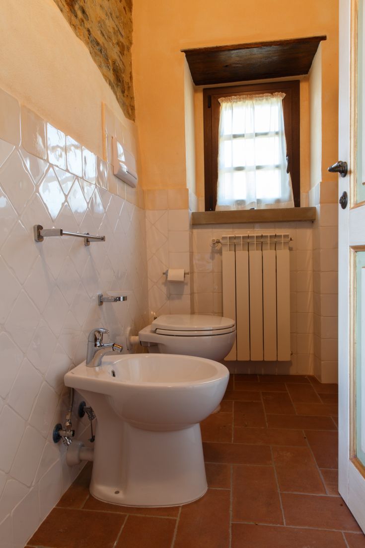 Heller Badezimmer mit weißen und terrakottafarbenen Fliesen, ausgestattet mit einem modernen Waschbecken und WC.