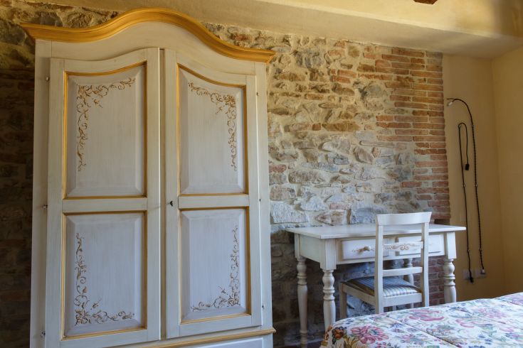 Ein gemütliches Zimmer mit einem einfachen Kleiderschrank und einem weißen Tisch. Die Steinwände schaffen eine rustikale Atmosphäre.