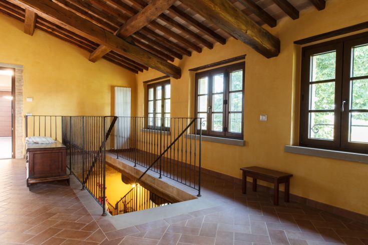 Innenraum eines Agriturismo mit gelben Wänden und sichtbaren Holzträgern, beleuchtet von großen Fenstern.