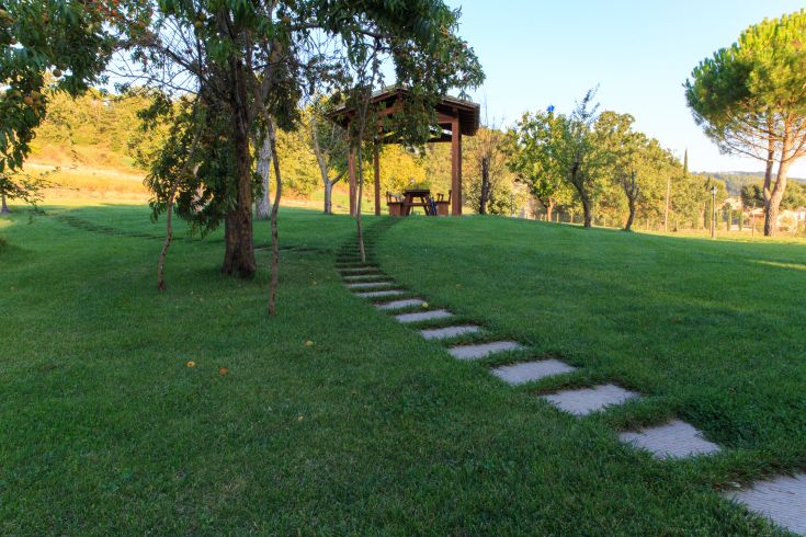 Ein Schotterweg führt zu einem Pavillon, der von Bäumen und üppigem Grün umgeben ist.