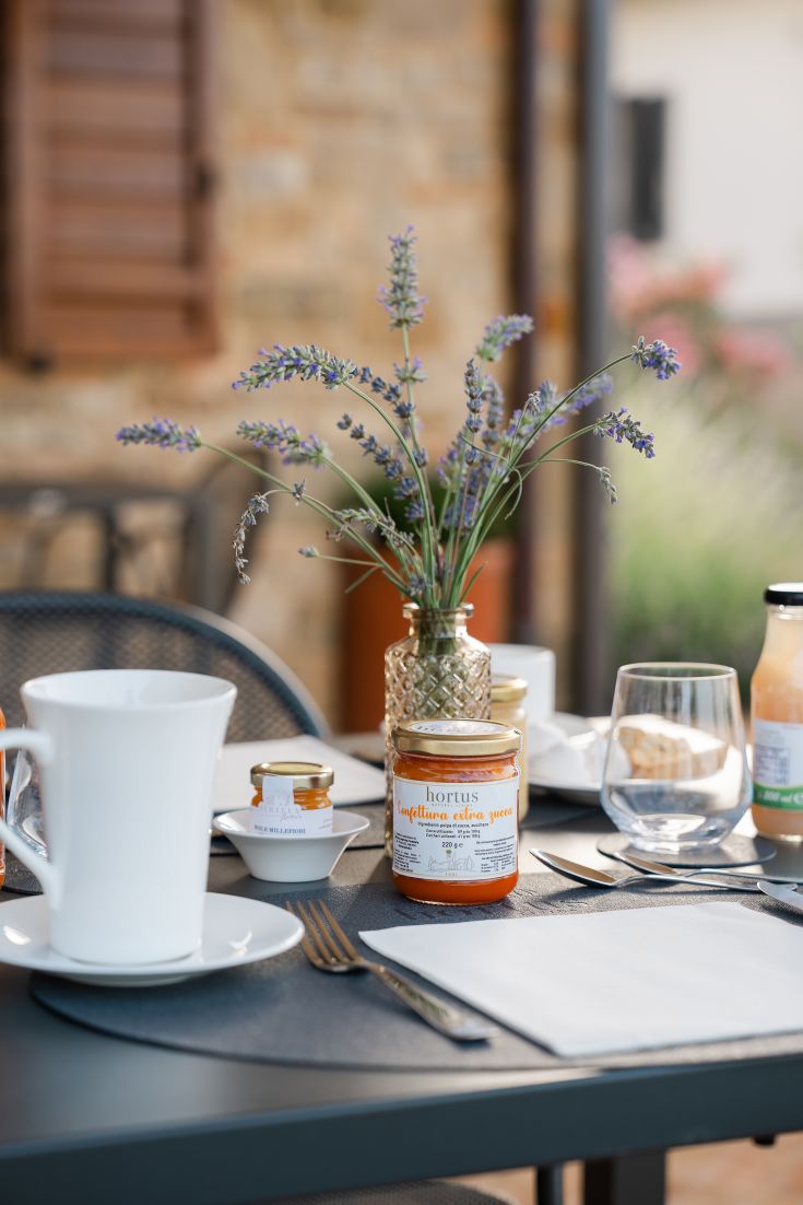 An outdoor table set with jams and a vase of lavender, surrounded by an agriturismo setting.