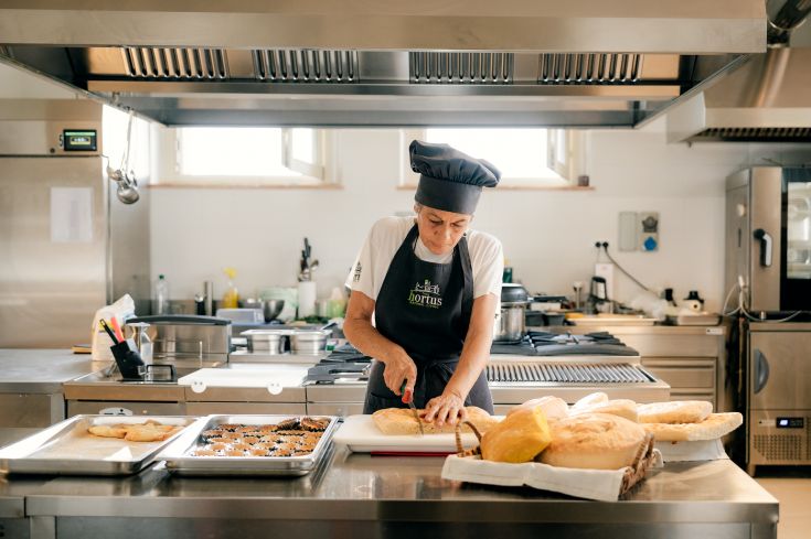 Inside an accommodation, a chef is cooking dishes with fresh, local ingredients. The environment is simple and tidy.