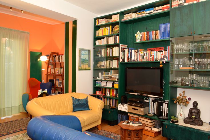 Un salon accueillant avec un canapé jaune et une bibliothèque colorée, créant une atmosphère calme.