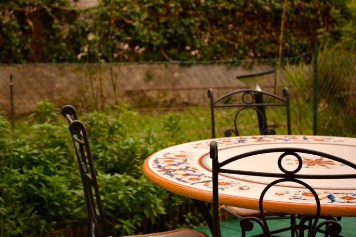 Une table en céramique décorée entourée de chaises, placée dans un jardin vert et paisible.
