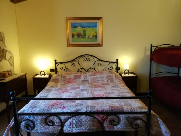 Ein einfaches Zimmer mit einem Doppelbett und Etagenbetten, beleuchtet von zwei modernen Lampen.