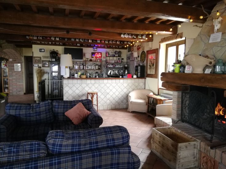 Gemütlicher Innenraum eines Agriturismo mit Barbereich, Sofas und einem angezündeten Kamin.