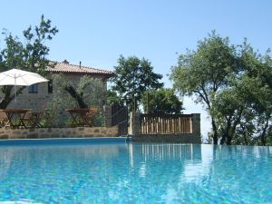 Szene eines klaren Swimmingpools mit Liegen und einem Sonnenschirm, umgeben von einem Steingebäude und Pflanzen.