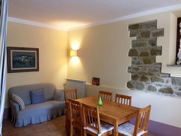 Cozy interior of a farmhouse with a wooden table and sofa, illuminated by warm lights and rustic details.
