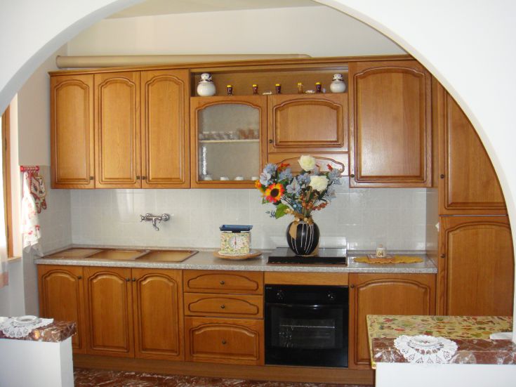 A simple, well-furnished kitchen with light wood furniture and green plants, perfect for sharing meals with others.