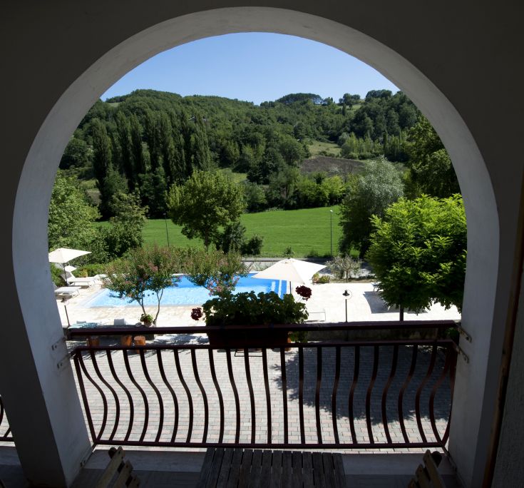 View of the pool and tranquil hills from a palace balcony surrounded by Umbrian greenery.