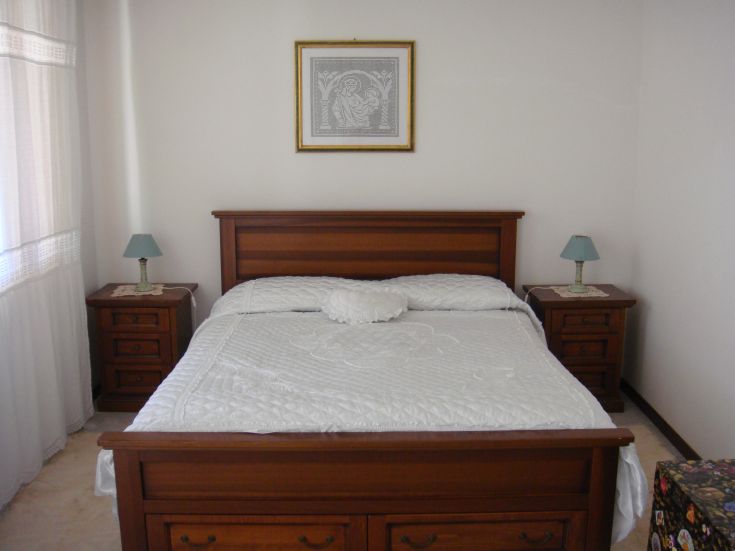 A simple bedroom featuring a double bed and wooden furniture, perfect for a peaceful stay.