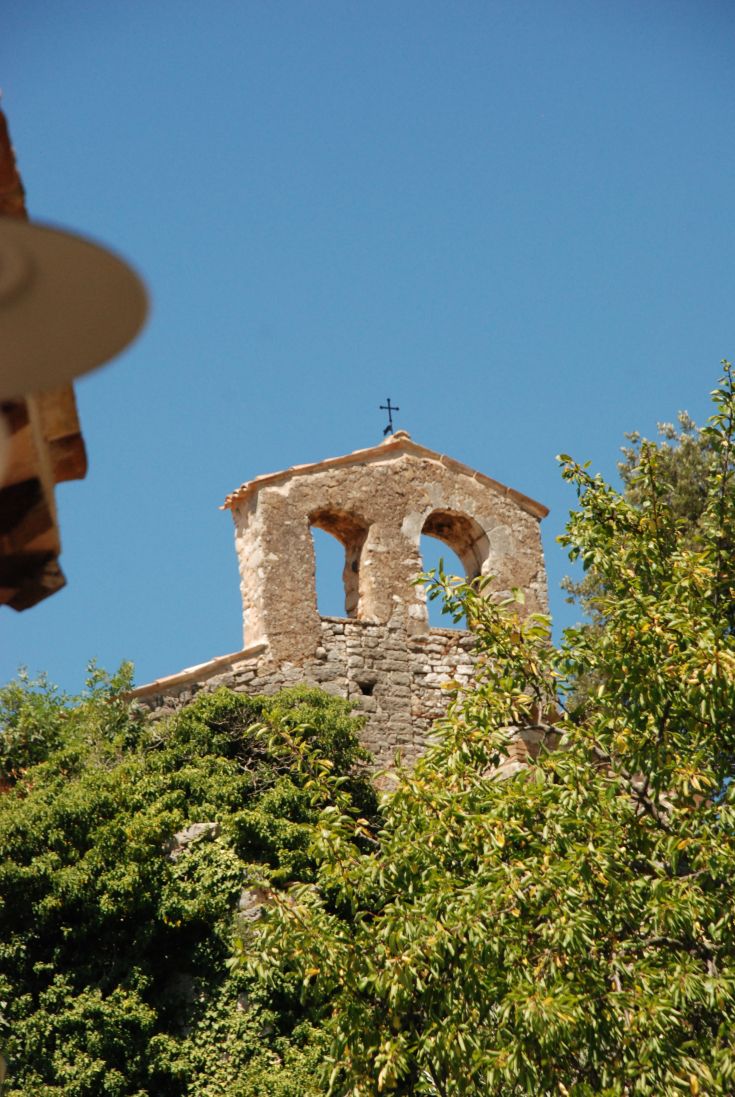 Un clocher situé dans un village désert, entouré de verdure sous un ciel dégagé.