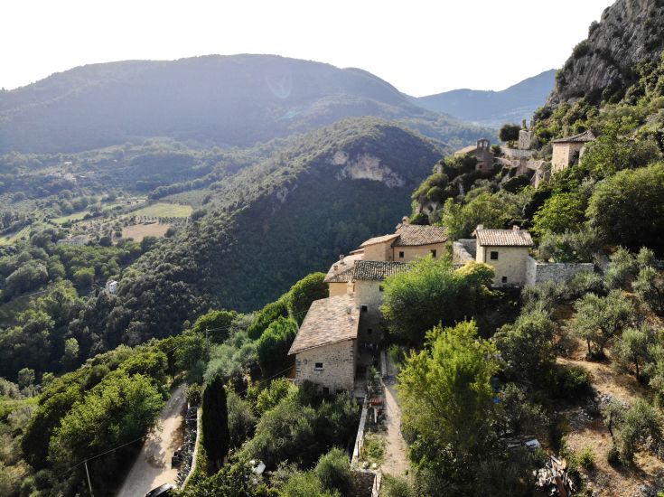 Un village médiéval bien conservé, avec des bâtiments en pierre entourés de verdure, dégageant une atmosphère paisible.