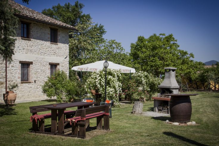 A relaxing outdoor area with tables and a barbecue, surrounded by greenery.