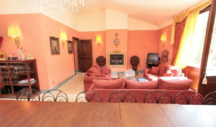 Soggiorno ampio con divani a strisce, ben illuminato da lampade e finestre affacciate su un paesaggio naturale.