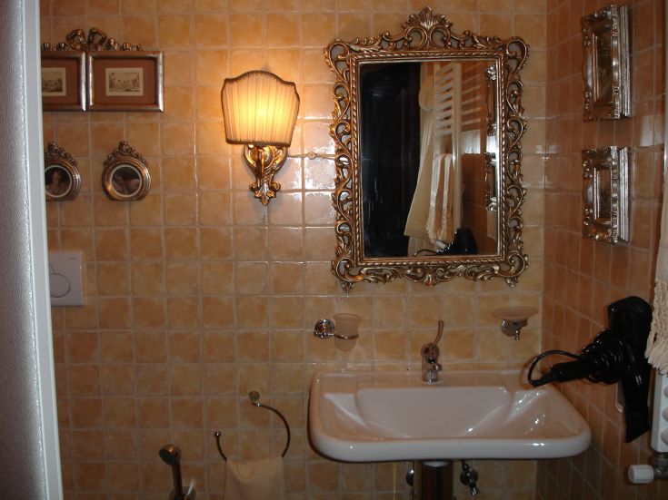 Bagno con piastrelle arancioni, specchio e illuminazione vintage.
