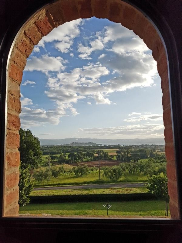 Una scena da una finestra che mostra colline e campi verdi sotto un cielo sereno.