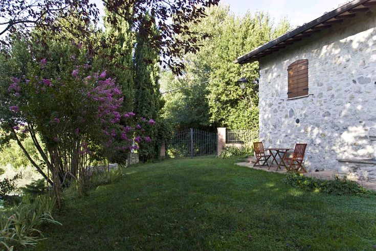 Panorama di un casale umbro circondato da un giardino con panchine, immerso nel verde.