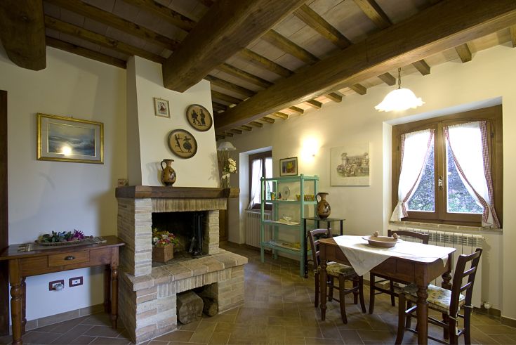 Interno semplice di un casale umbro, con un camino e mobili in legno tra cui un tavolo e una sedia.