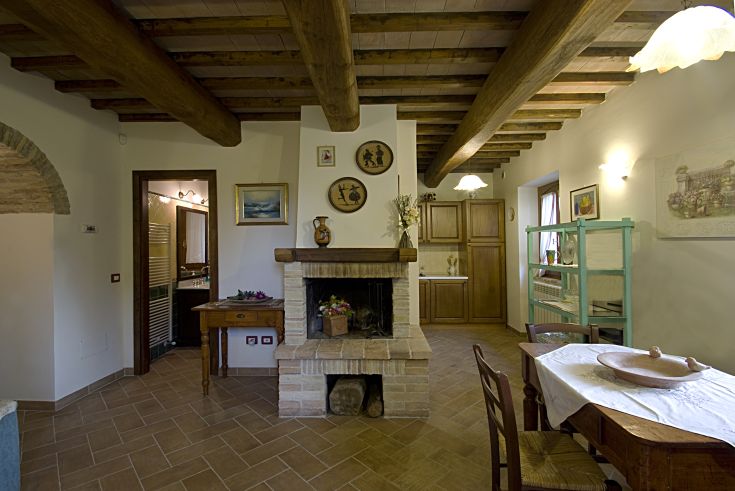 Interno di un casale con travi a vista e un camino, spazio ideale per momenti di relax.